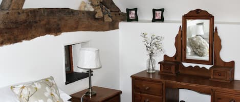 A bedroom with a wooden headboard, a bed with white bedding, a nightstand with a lamp, a dresser with drawers, and a mirror.