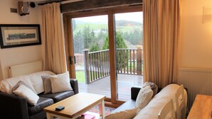 Una sala de estar acogedora con un sofá, una mesa de centro y vistas a una terraza y follaje exterior.