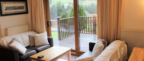Una sala de estar acogedora con un sofá, una mesa de centro y vistas a una terraza y follaje exterior.