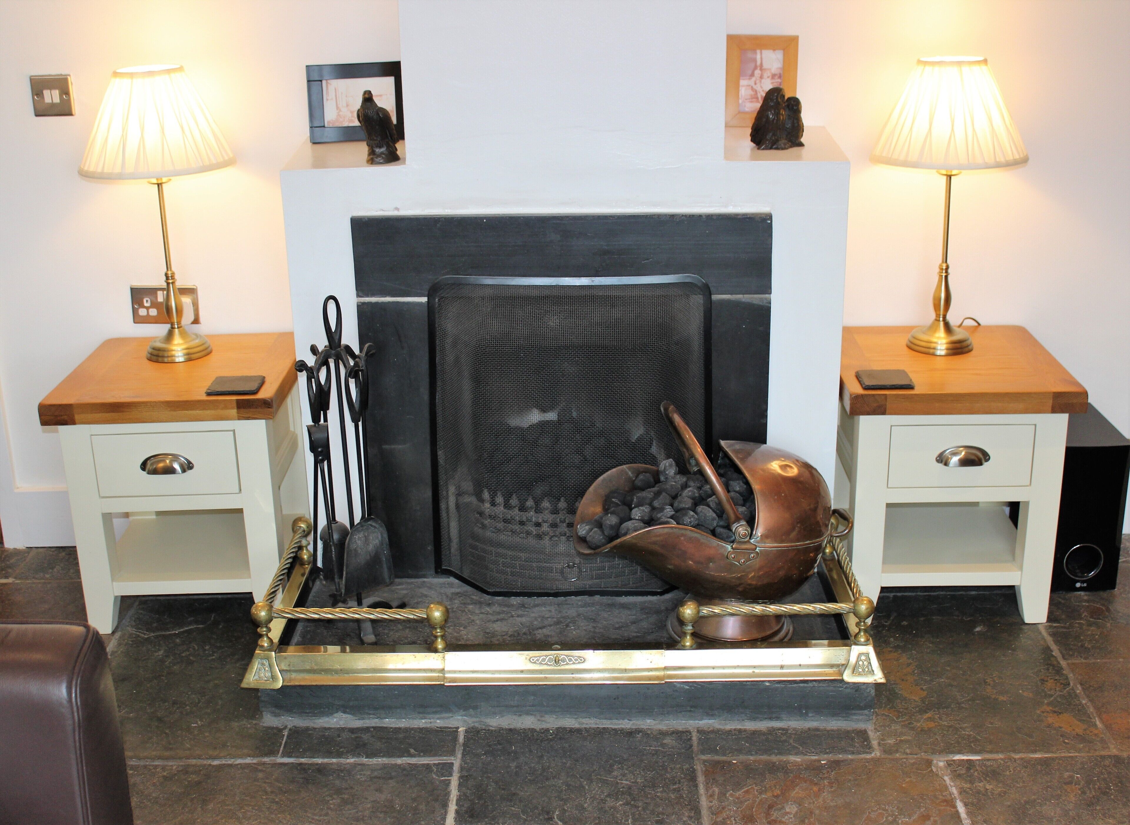 A bedroom with a bed, two bedside tables, a lamp on each table, a fireplace, and a decorative metal tray.