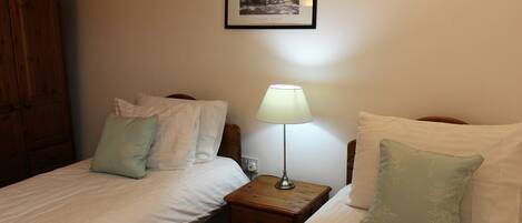 A bedroom with two beds, a wooden nightstand with a lamp, a framed photo on the wall, and a wooden wardrobe.