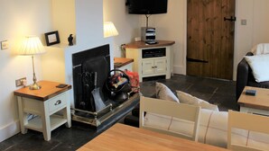 Una sala de estar con chimenea, televisor montado en la pared, una puerta de madera y una mesita con lámpara.
