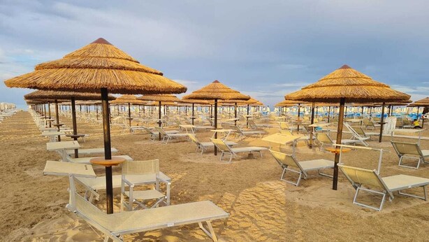 Une plage bordée de rangées de chaises longues et d’ombrelles en chaume, évoquant l’atmosphère d’un complexe hôtelier balnéaire.