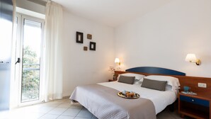 Une chambre d’hôtel avec un lit, une table de chevet, un plateau de pâtisseries et une vue par la fenêtre.