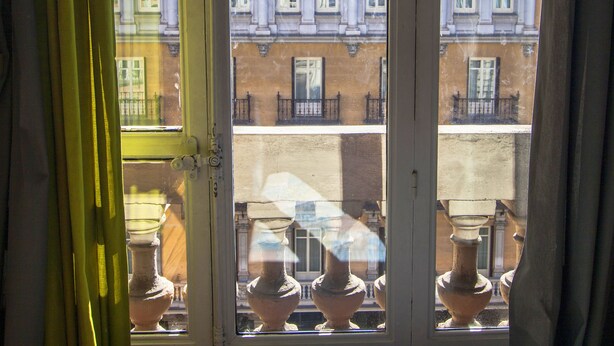Ein Zimmer mit großem Fenster, das auf ein Gebäude mit Balkonen und aufwendiger Architektur blickt.