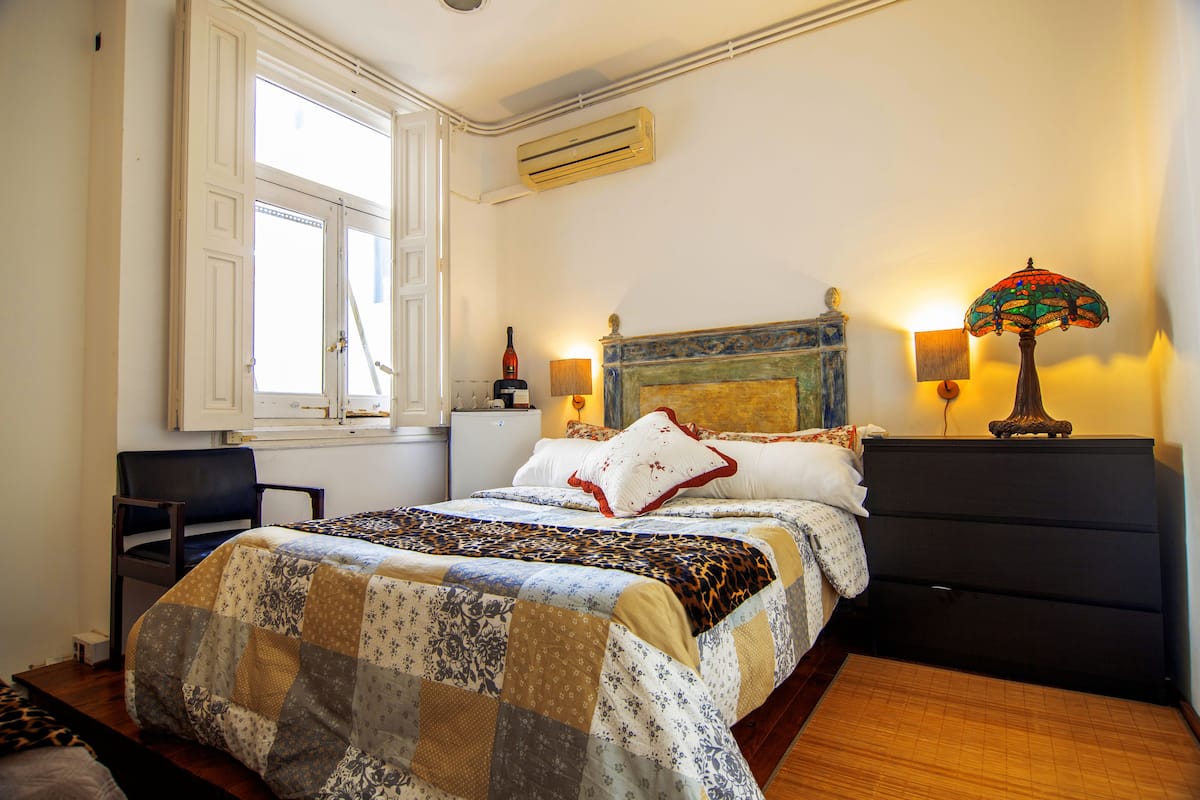 Une chambre à coucher avec un lit, une chaise, une commode, une lampe et une fenêtre.