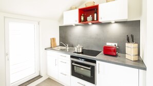 Una cocina moderna con armarios blancos, horno empotrado, tostadora roja y pileta.