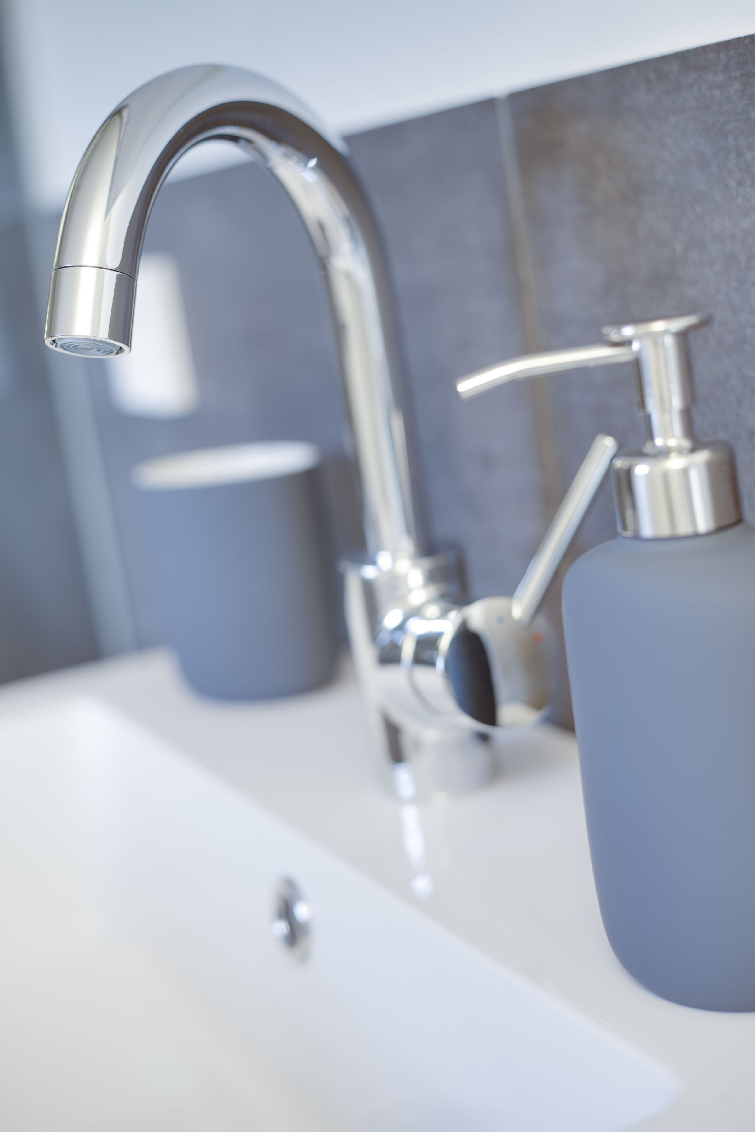 A modern bathroom with a chrome faucet, a soap dispenser, and a cup.