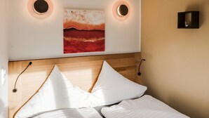 Una cama bien hecha con almohadas blancas y oscuras, un cabecero de madera y dos lámparas fijadas a la pared.