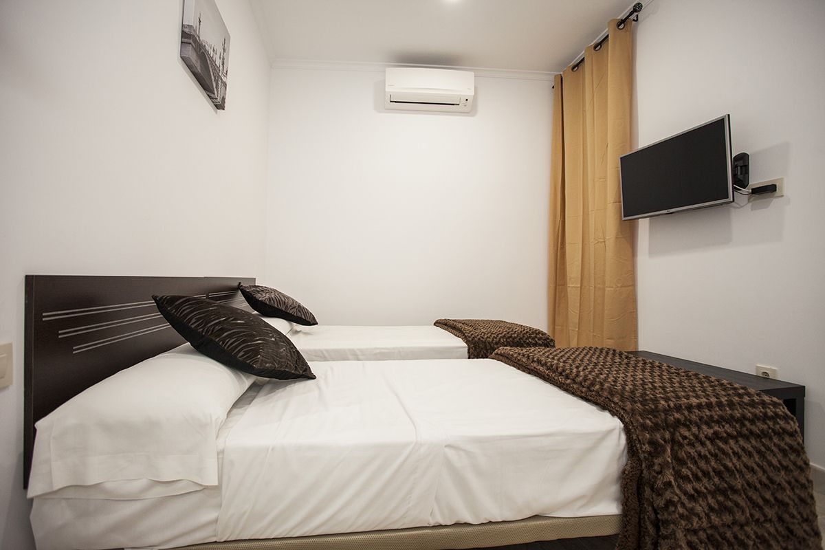 Une chambre avec deux lits, un téléviseur fixé au mur, un appareil de climatisation et un tableau encadré accroché au mur.