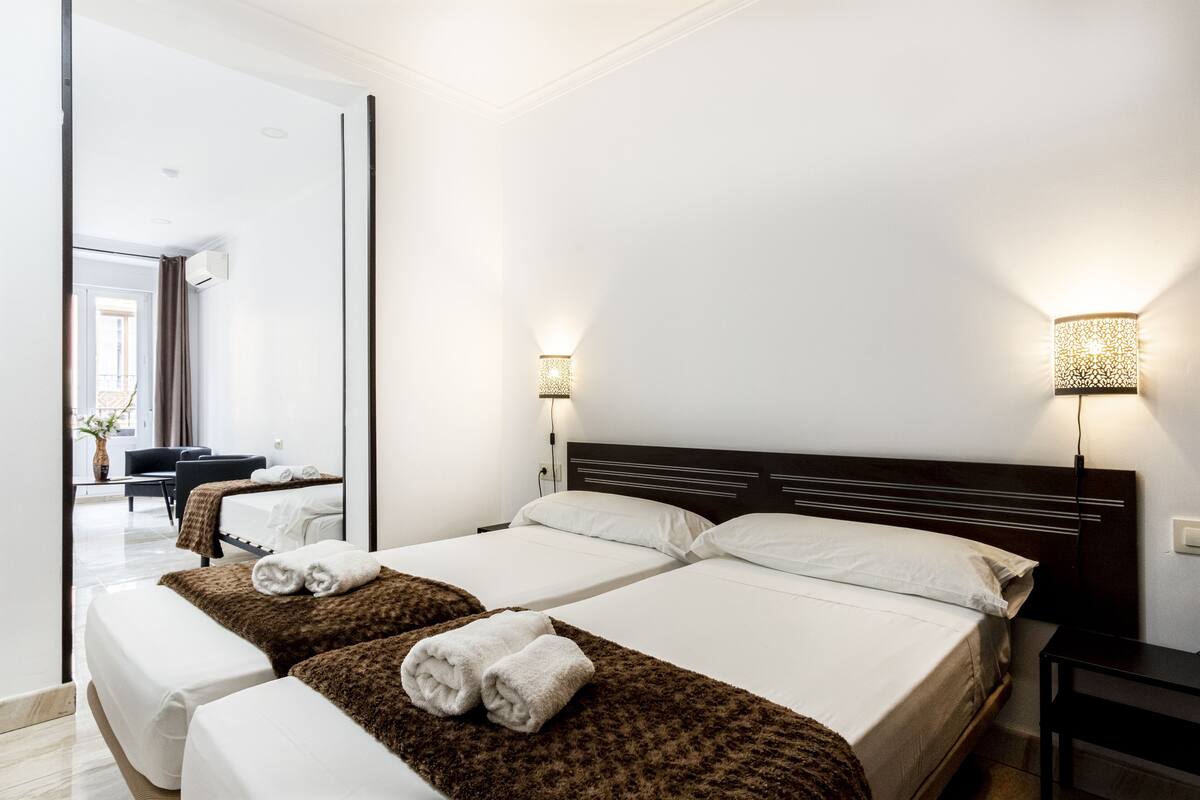 Hotellihuone, jossa on kaksi sänkyä, oleskelualue tuolilla sekä suuri peili.