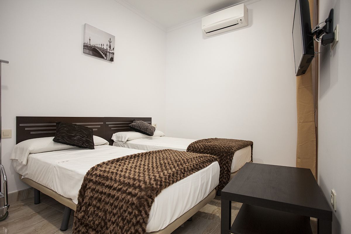 A hotel room with two beds, a small table, an air conditioning unit, and a picture on the wall.