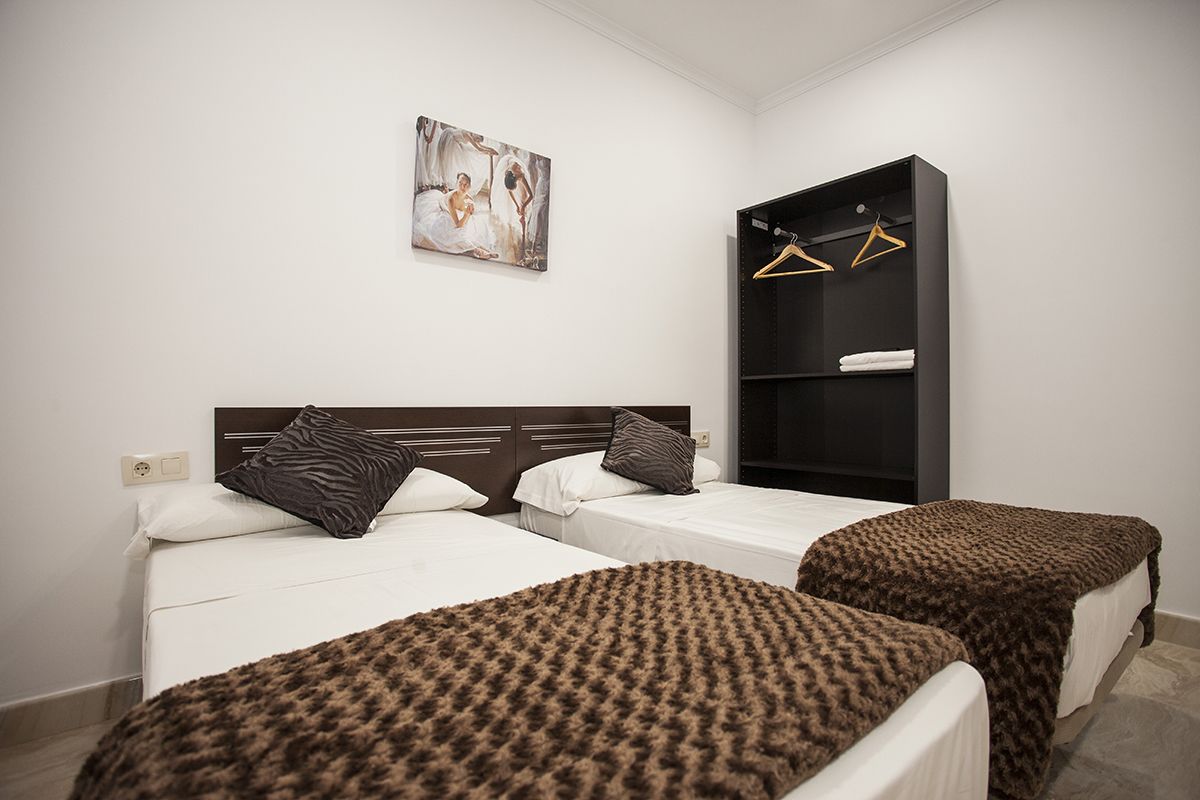 Habitación de hotel con dos camas, una colcha de estampado de cebra en una de ellas, un cuadro en la pared y un armario negro con perchas.