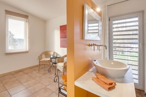 Une salle de bain avec un grand lavabo blanc, un miroir et une fenêtre avec des stores.