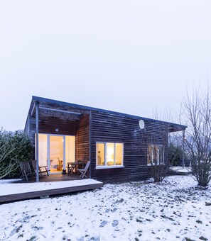 Una casa moderna de madera con un porche cubierto, ventanas amplias y un patio cubierto de nieve.