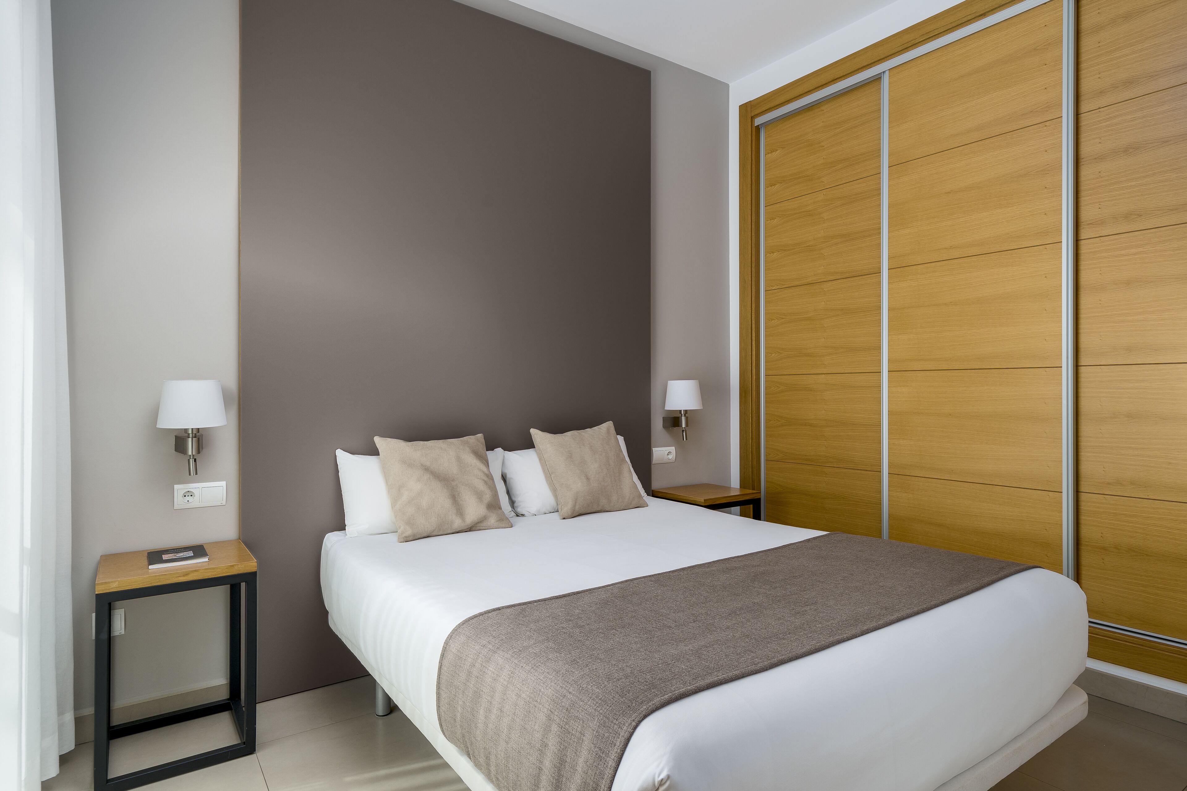 Een moderne hotelkamer met een groot bed, twee nachtkastjes met lampen, en een houten garderobe.