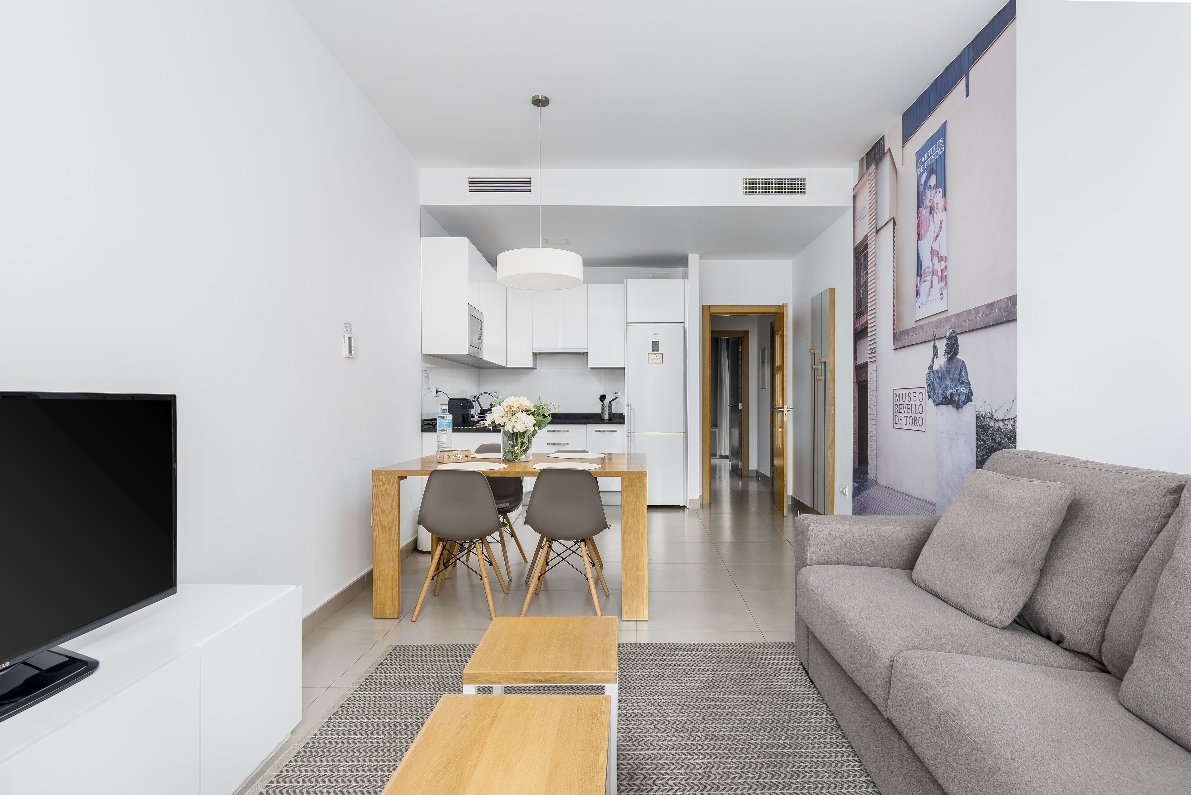 Een moderne woonkamer met een flatscreen televisie, een bank en een eethoek met een tafel en stoelen.