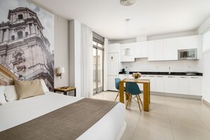 Et hotelværelse med en seng, et skrivebord, en stol, et tekøkken med skabe og en mikroovn, samt et stort vægmaleri.