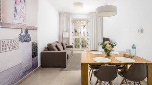 A modern living room with a sofa, a dining table with chairs, and a large window. - Suites del Pintor Historial Center, by Hoteles con Cultura (Málaga)