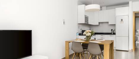 Una cocina moderna con armarios blancos, una mesa de comedor con sillas y un televisor sobre un mueble.