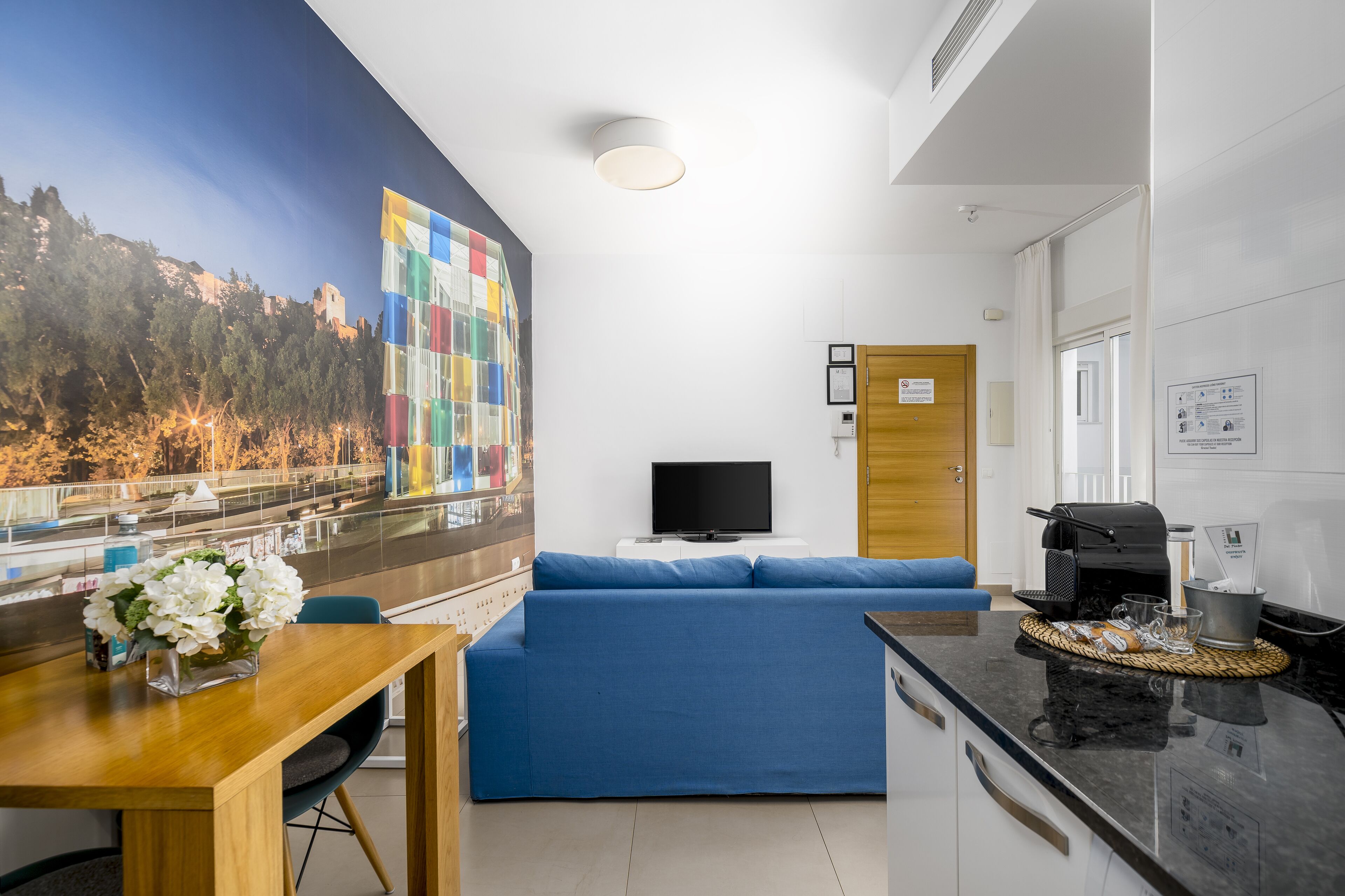 Una sala de estar moderna con un sofá azul, una mesa de comedor de madera y un televisor de pantalla plana.