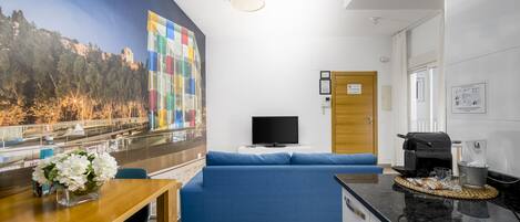 Una sala de estar moderna con un sofá azul, una mesa de comedor de madera y un televisor de pantalla plana.