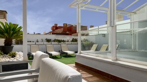 A modern outdoor seating area with a glass enclosure, white cushioned chairs, and a potted plant. - Suites del Pintor Historial Center, by Hoteles con Cultura (Málaga)