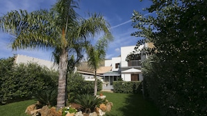 Un jardín bien cuidado con palmeras y arbustos, un patio y un edificio moderno con un balcón.