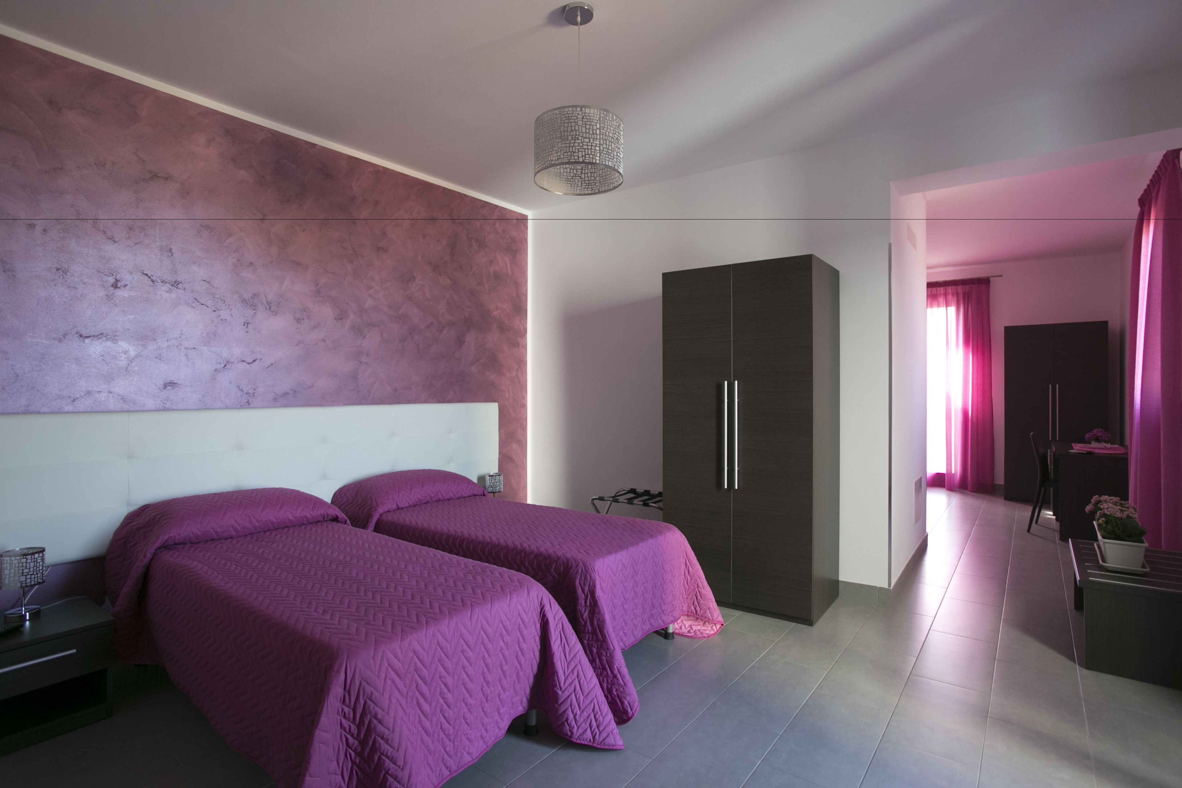 A modern bedroom with two beds, a wardrobe, and a small table with a plant.