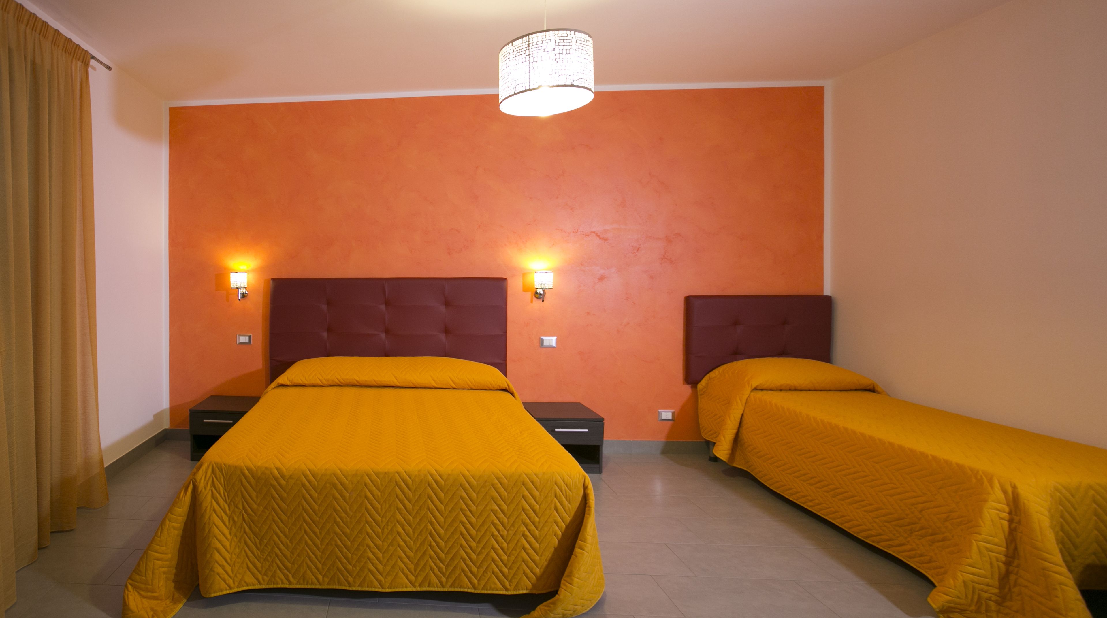 A hotel room with two beds, orange walls, and two wall-mounted lights.
