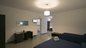 Una habitación de hotel moderna con una cama, escritorio, silla y televisor en la pared.