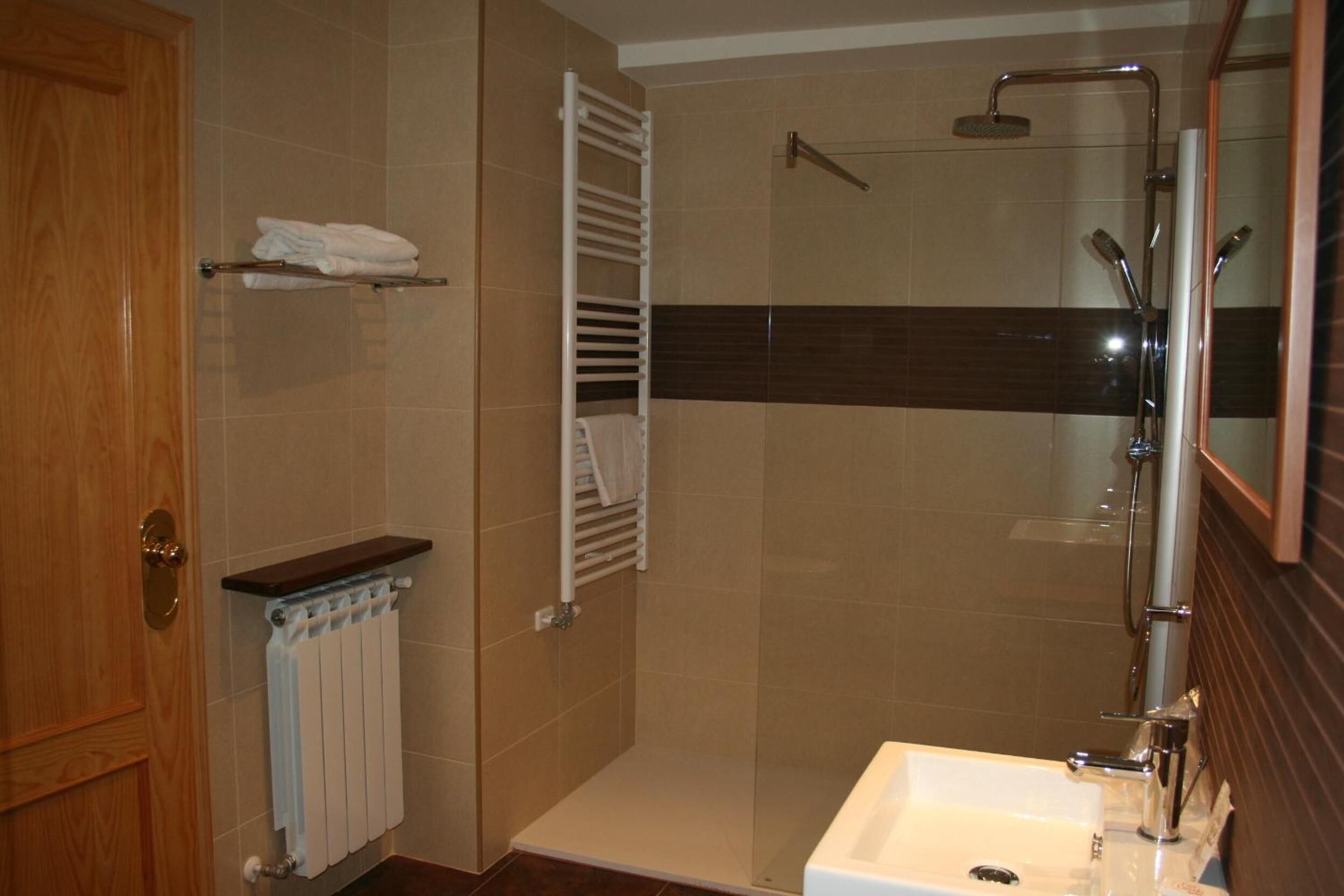 Un baño con ducha, lavamanos, toallero y radiador.