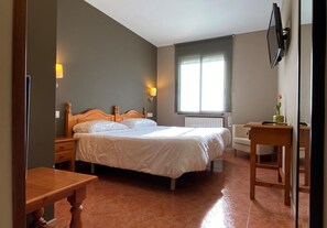 A bedroom with a large bed, bedside tables, a desk, a chair, a window with blinds, and a wall-mounted TV. - Hotel Casa Custodio (Isabena)