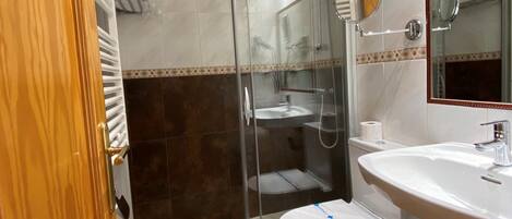 A bathroom with a glass-enclosed shower, a toilet, and a sink.