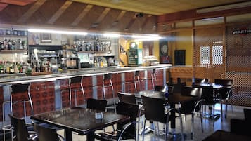 Una zona de bar con mesas y sillas, una barra con diferentes botellas y un dardo en la pared.