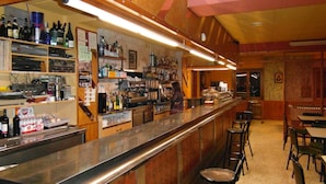 A bar area with a long counter, shelves with bottles and glasses, and a seating area with tables and chairs. - Hotel Casa Custodio (Isabena)