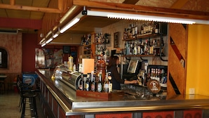 A bar area with a counter, shelves of bottles, and stools. - Hotel Casa Custodio (Isabena)