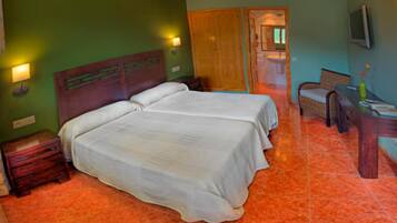 Quarto com duas camas, cabeceira de madeira, mesa de cabeceira, escrivaninha com cadeira e televisão na parede.