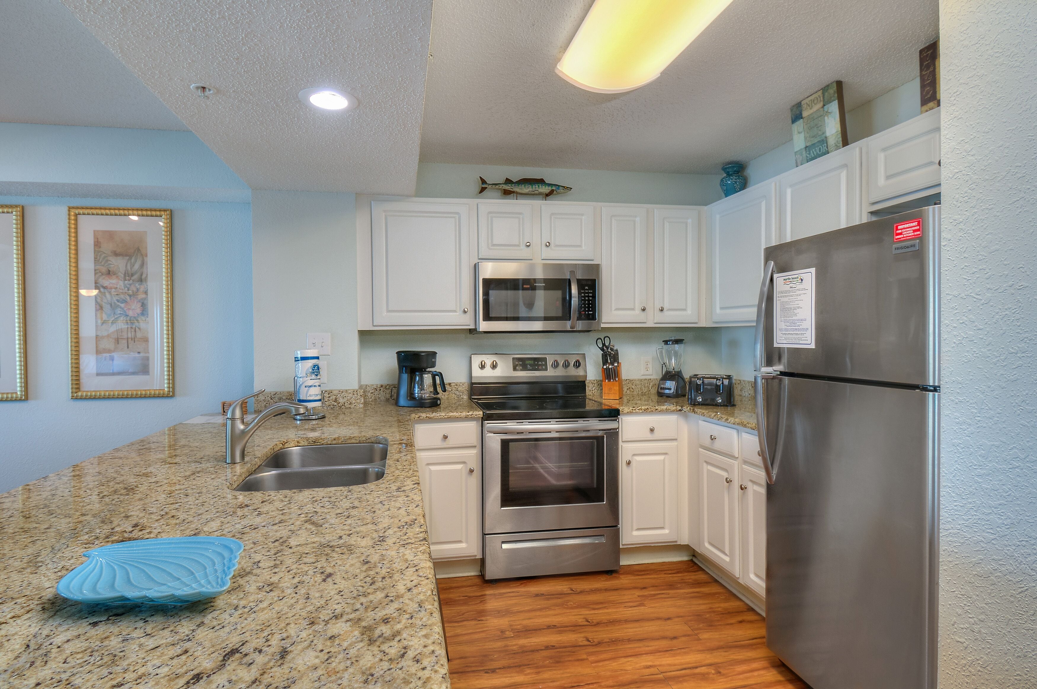 A kitchen with white cabinets, stainless steel appliances, a granite countertop, and a blue decorative plate.