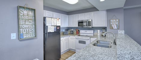 Una cocina con gabinetes blancos, un refrigerador negro, un microondas, una estufa y encimeras de granito.