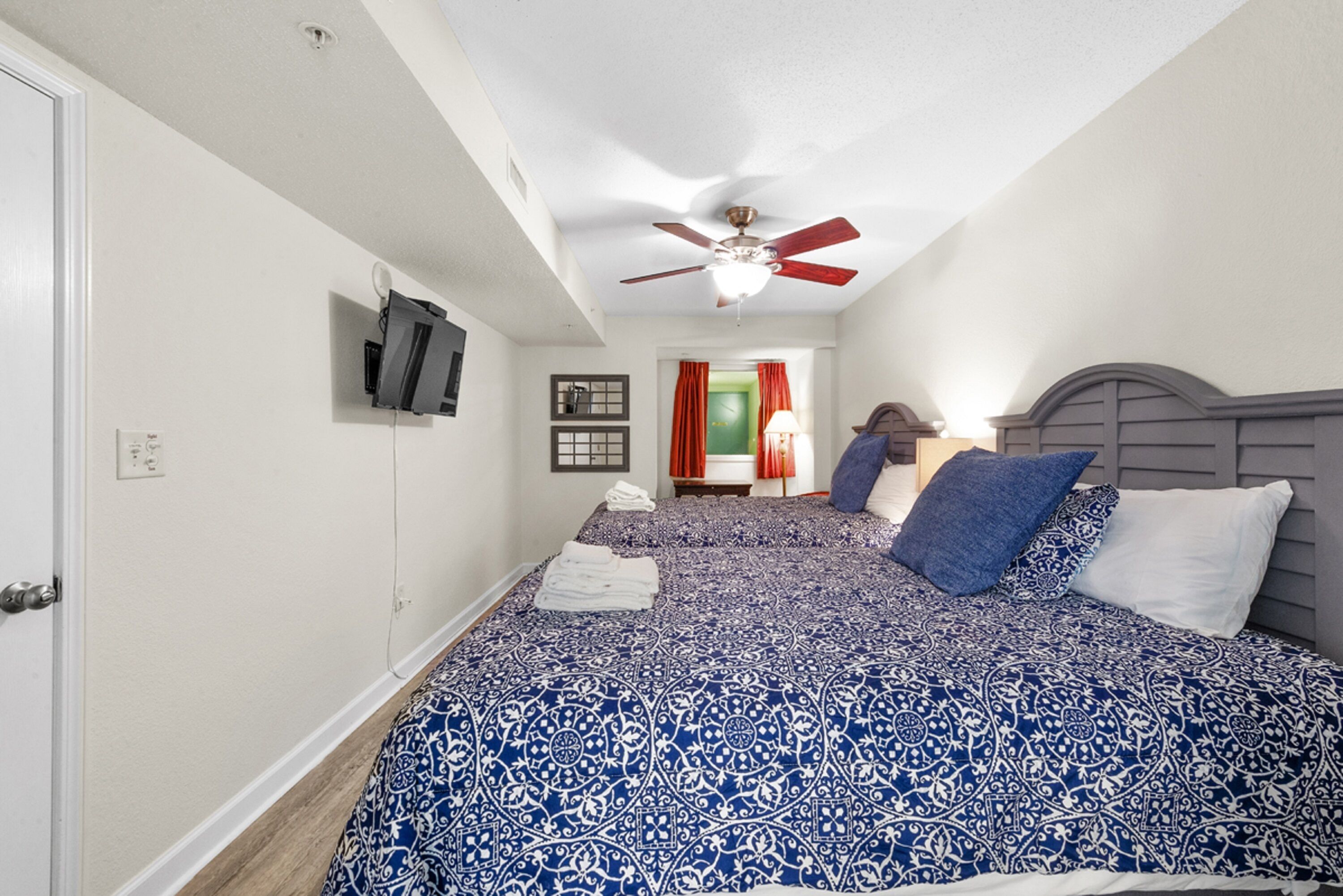 Quarto com cama grande, ventilador de teto e televisão na parede.