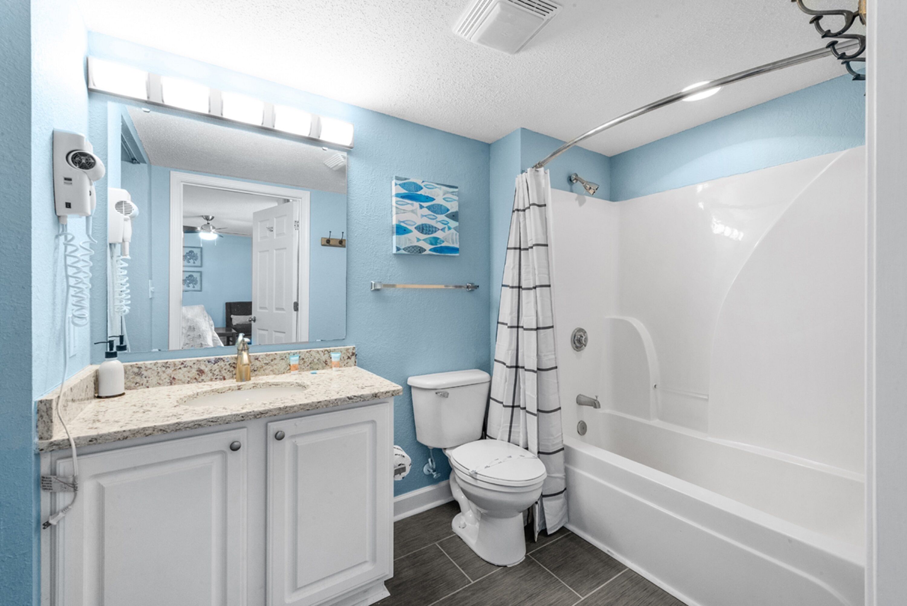 A bathroom with a white toilet, a bathtub, a shower curtain, and a vanity with a mirror.