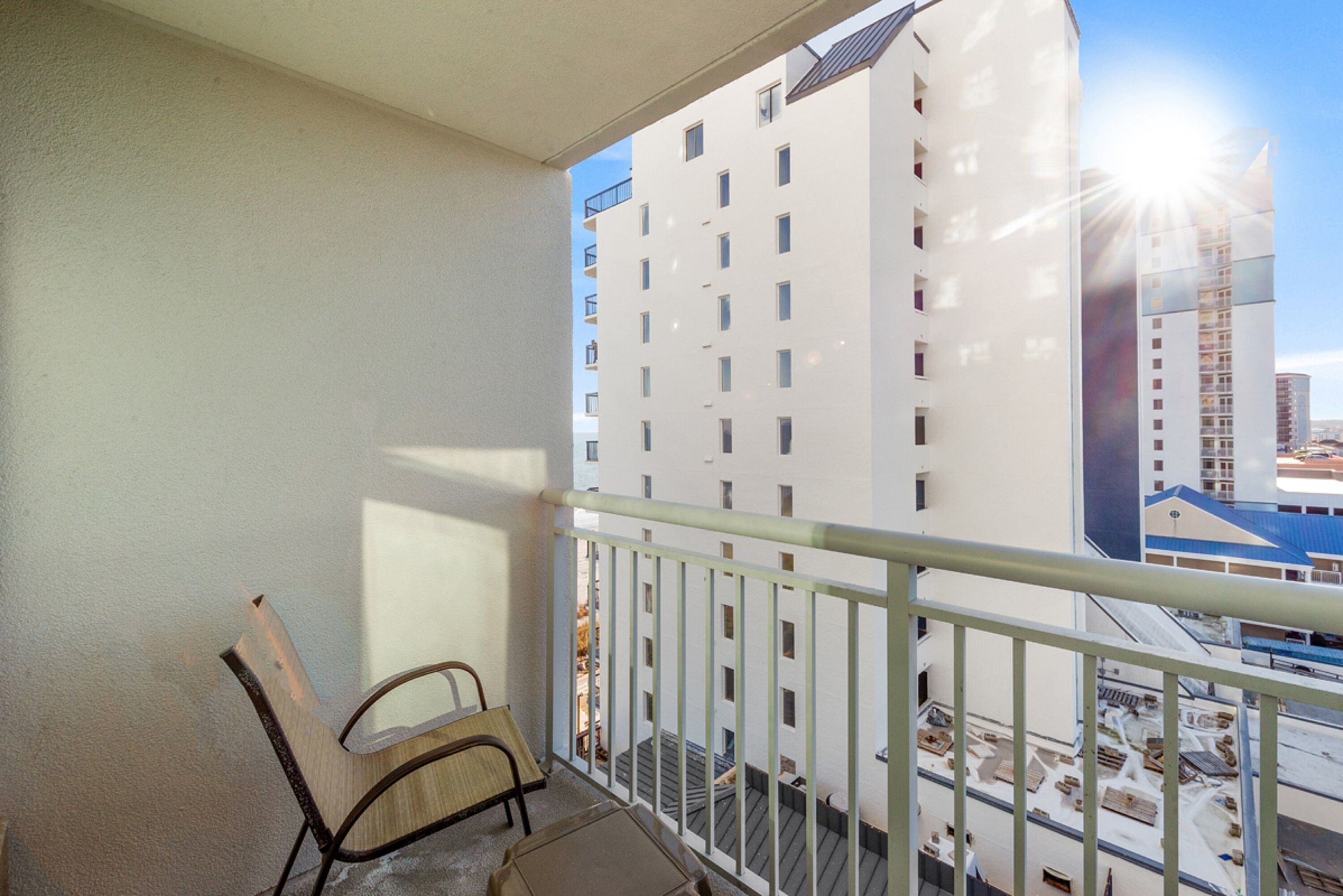 A balcony with a chair and a table, overlooking a building with multiple windows and a clear sky.