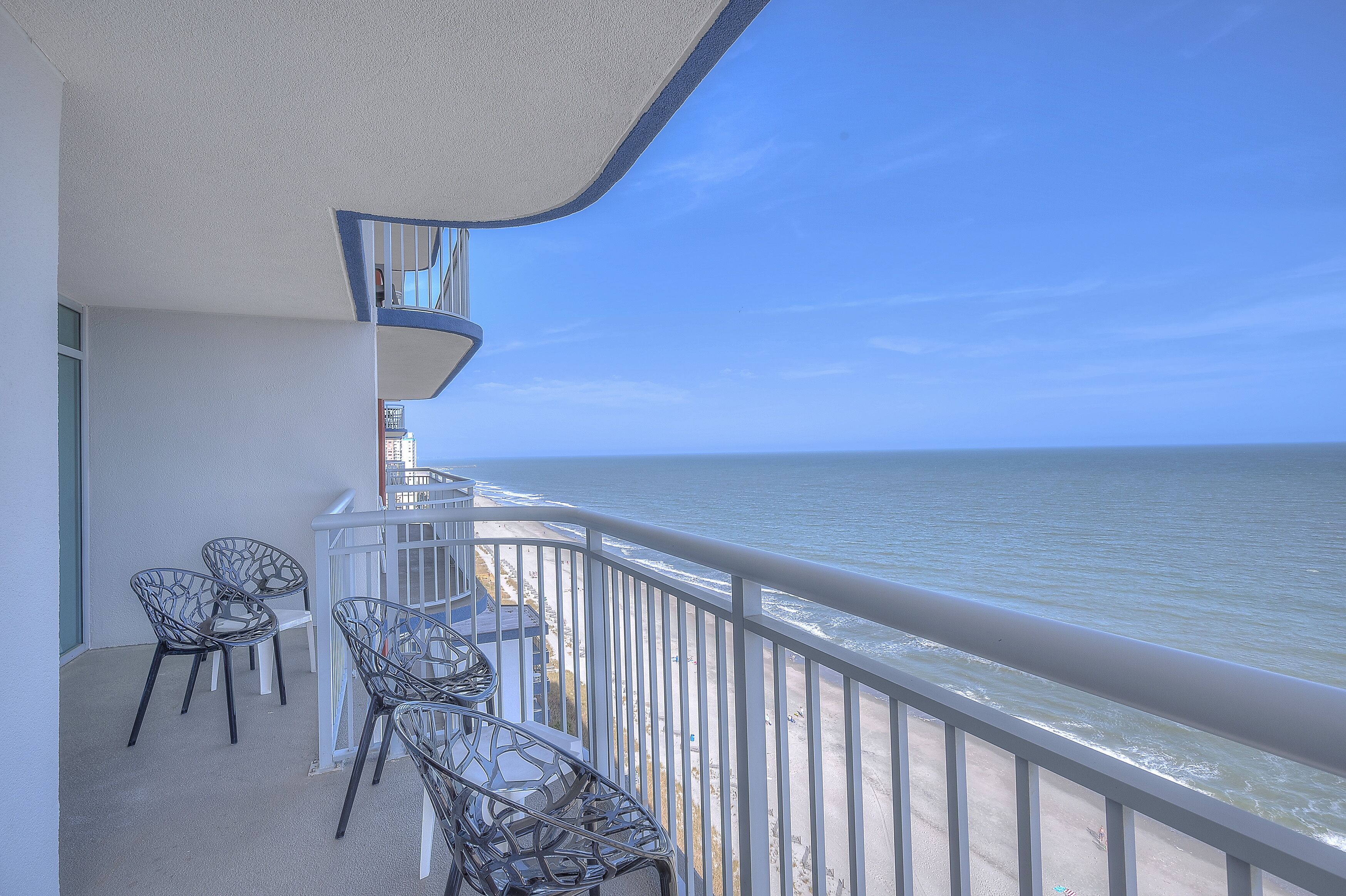A balcony with metal chairs and a railing overlooking a beach.