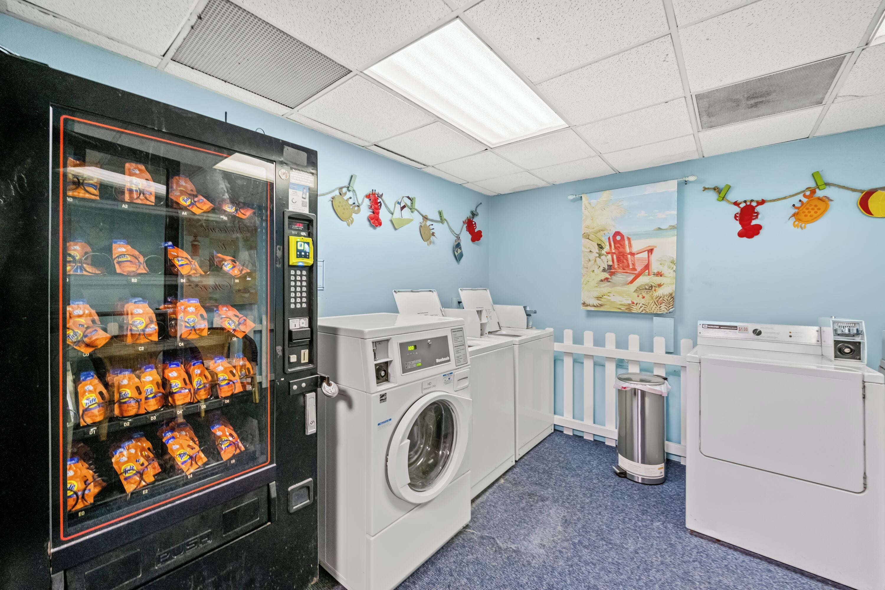 A laundry room with a vending machine, washing machines, and a trash can.