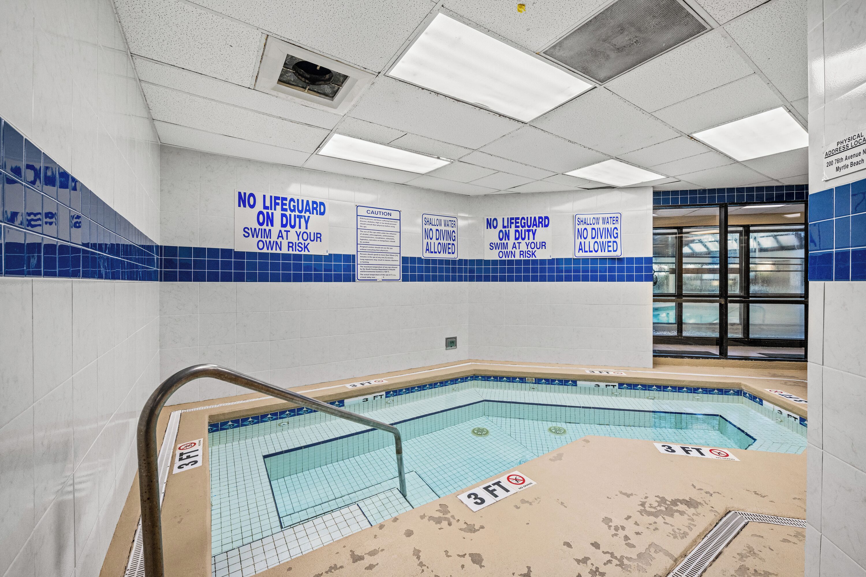 A swimming pool area with safety signs, a 3 FT depth marker, and a tiled wall.