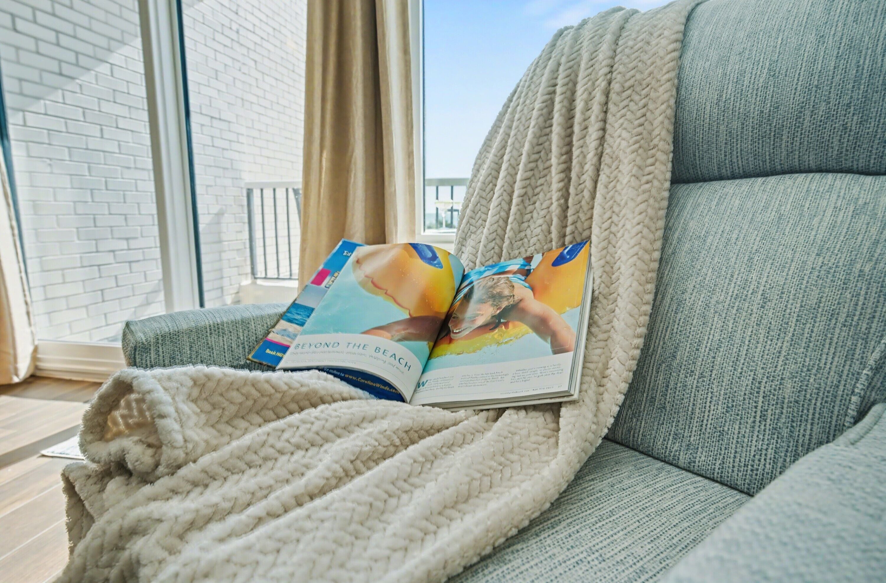 A magazine on a couch with a view of a balcony and a brick wall.