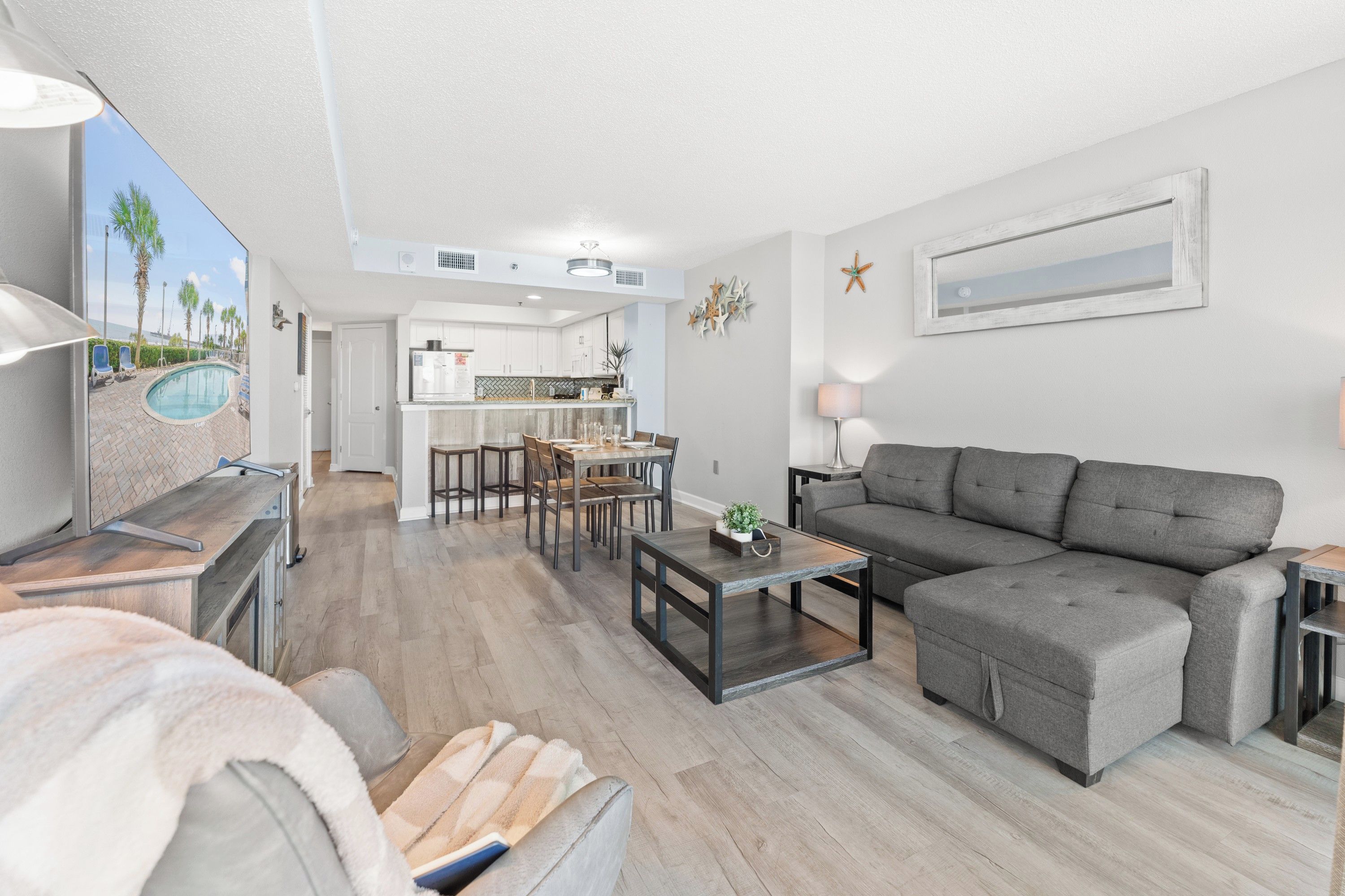 Ein modernes Wohnzimmer mit grauem Sofa, einem Essbereich mit Tisch und Stühlen und einer Küche im Hintergrund.