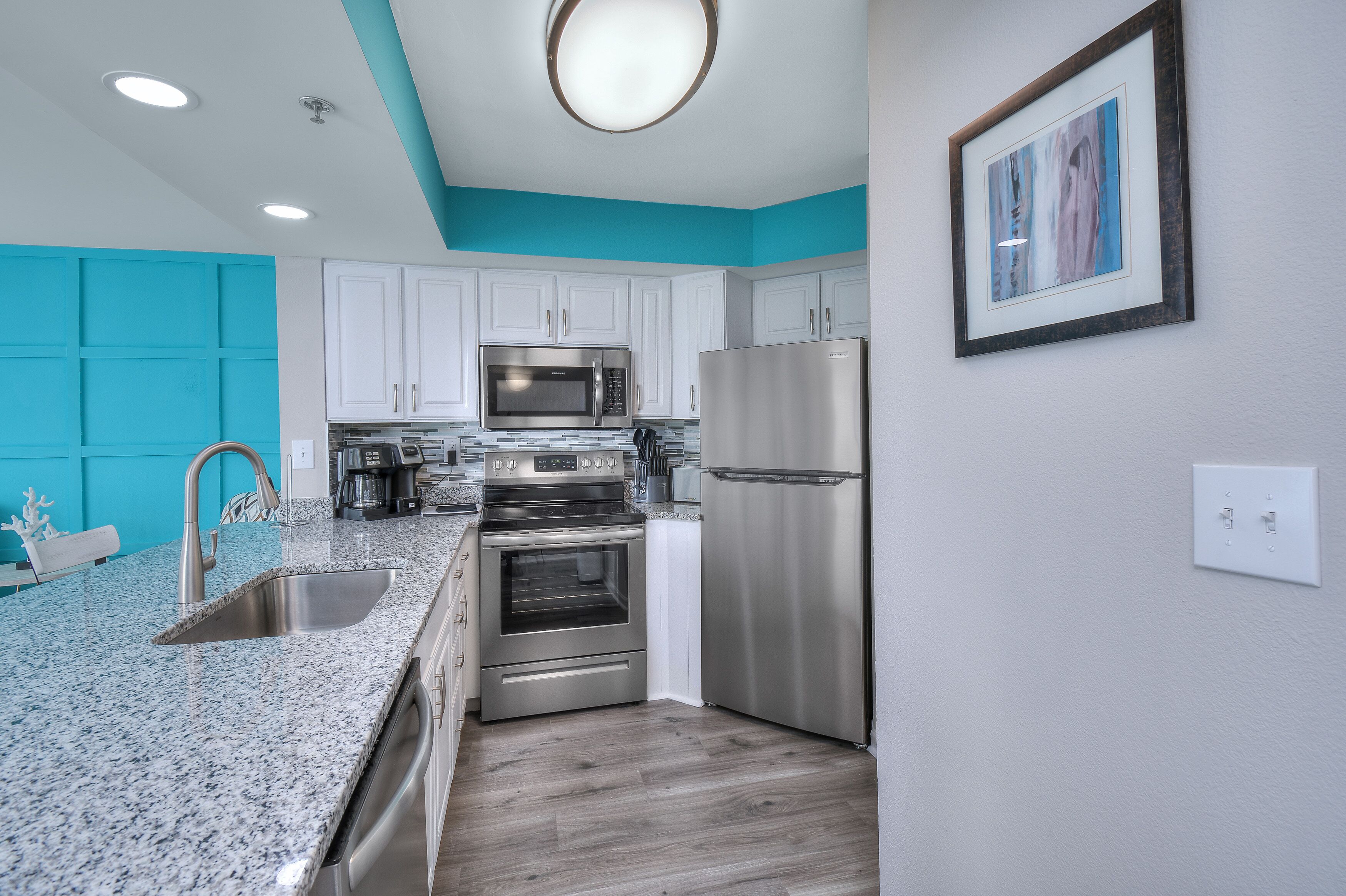 A modern kitchen with white cabinets, stainless steel appliances, a granite countertop, and teal accent walls.