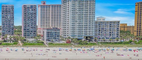 A beachfront hotel with multiple high-rise buildings, a sandy beach, and umbrellas.
